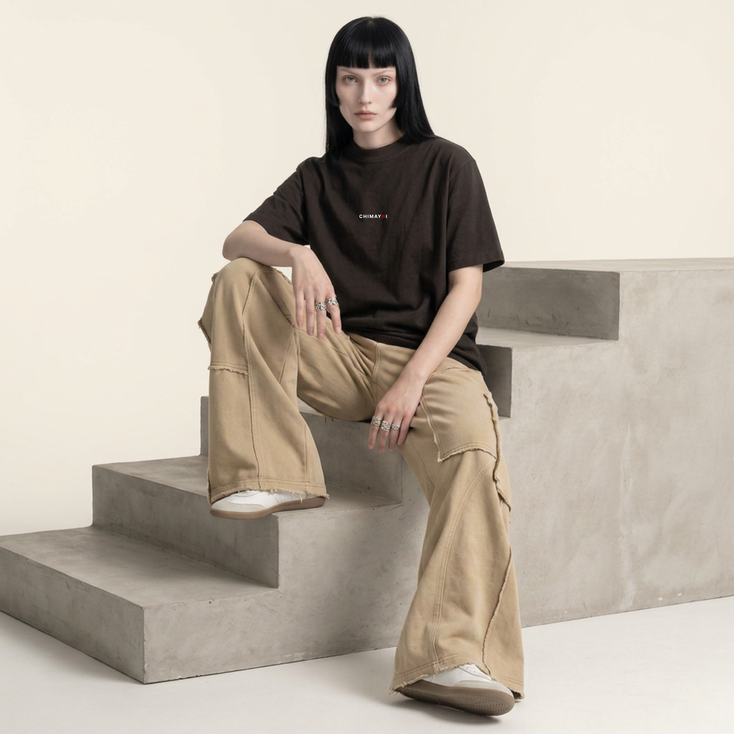 Female model wearing CHIMAYOI Black oversized cropped tee sitting on concrete steps, representing modern minimalist fashion.